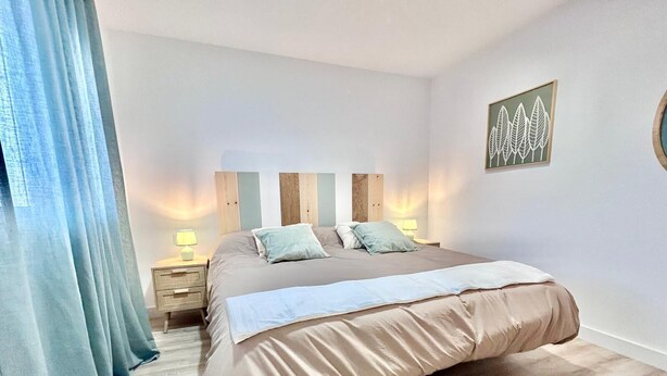 Une chambre à coucher avec un grand lit, une table de chevet avec une lampe, une tête de lit en bois et une œuvre d’art murale.