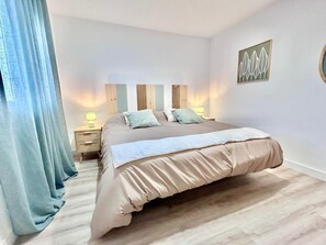 A bedroom with a large bed, a nightstand with a lamp, a wooden headboard, and a wall art piece. - Baélia Casa Nerea (Alicante)