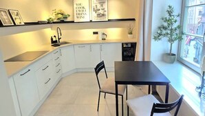 A modern kitchen with white cabinets, a black countertop, and a dining table with chairs. There are two framed pictures on the wall, a potted plant by the window, and a coffee machine on the counter. - Riga Stylish Old Town getaway next to Dome square (Rīga)