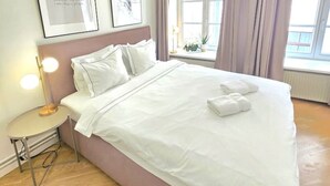 A neatly made bed with white linens, a bedside lamp, and two framed pictures on the wall. - Riga Stylish Old Town getaway next to Dome square (Rīga)