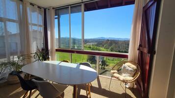 Een balkon met een tafel en stoelen, een rieten stoel en uitzicht op een groen landschap.