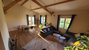 Un vaste espace de vie doté d’un haut plafond, de poutres en bois, d’une table à manger avec des chaises, d’un canapé, d’une petite table basse et d’une grande fenêtre offrant une vue sur l’extérieur.