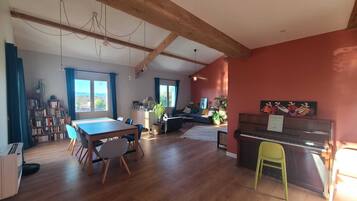 Een ruime woonkamer met een eettafel, stoelen, een piano en een boekenkast.
