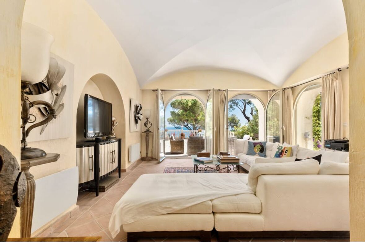A spacious living room with a large bed, a television, and a view of the outdoors through arched windows.