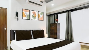 Une chambre d’hôtel avec un grand lit, une armoire en bois, un téléphone et trois œuvres d’art encadrées accrochées au mur.