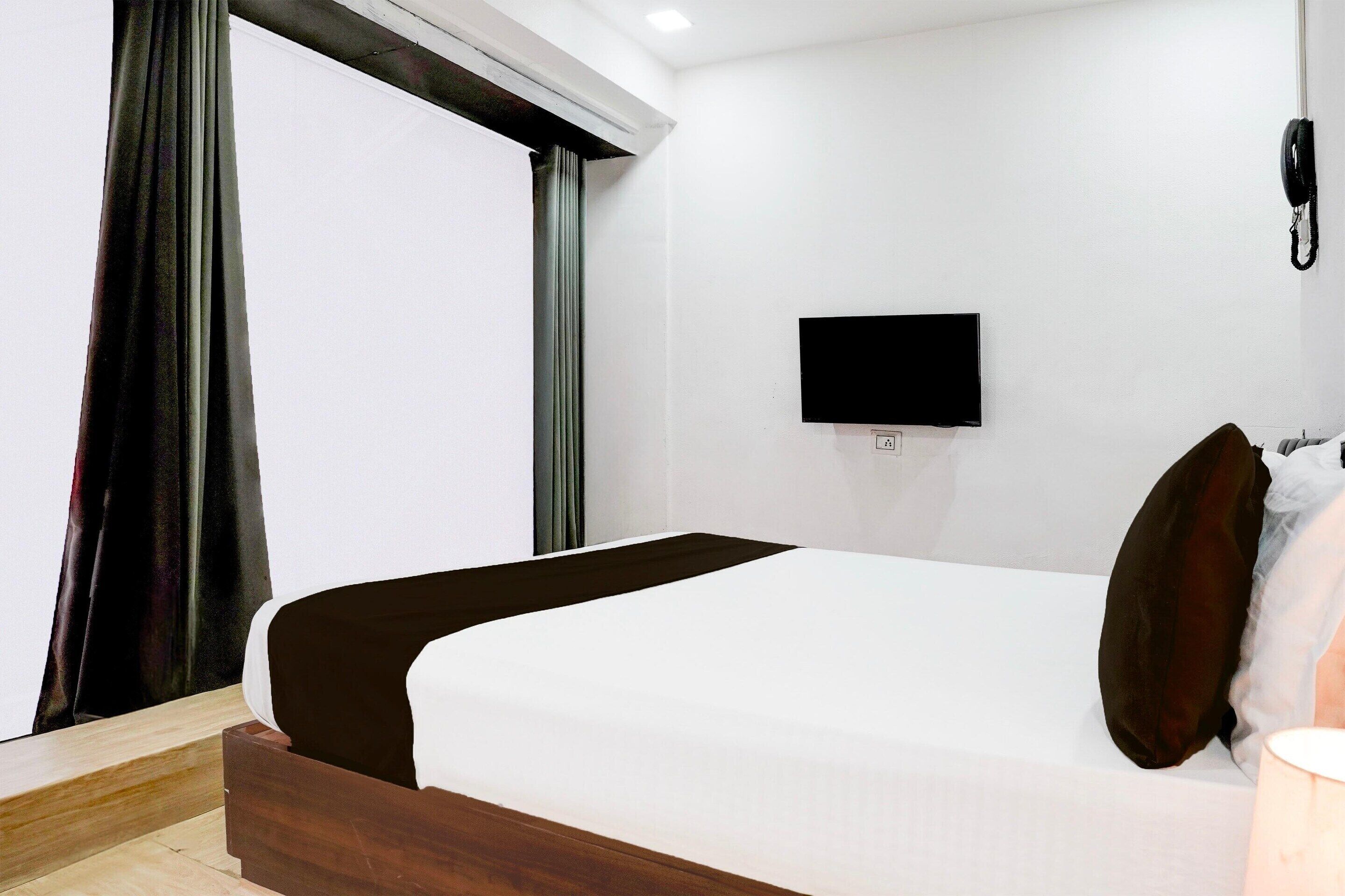 A hotel room with a bed, a flat-screen TV mounted on the wall, and a telephone.