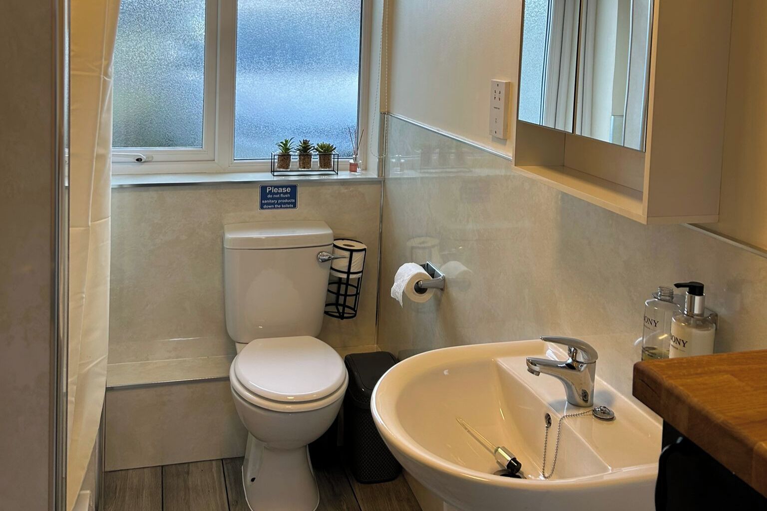 A small, clean bathroom with a toilet, sink, and a window above the toilet.