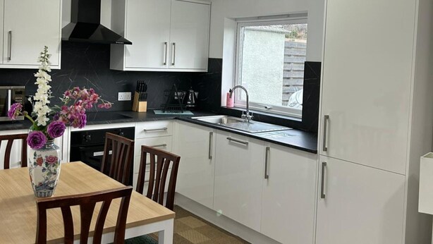 A modern kitchen with white cabinets, a black stove hood, and a window providing natural light. - Hot tub - Garden - Bbq - Parking - Pets - Sleeps 6 (Strathpeffer)