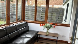A room with a black leather sofa, a wooden bench, and a vase of flowers on a small table. - Hot tub - Garden - Bbq - Parking - Pets - Sleeps 6 (Strathpeffer)