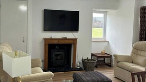 A living room with a fireplace, a television mounted on the wall, and a sofa. - Hot tub - Garden - Bbq - Parking - Pets - Sleeps 6 (Strathpeffer)