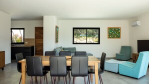 Una sala de estar moderna con una mesa de comedor de madera, sillas negras, un sofá color turquesa y un ventanal con vistas a los árboles.