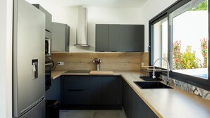 Una cocina moderna con horno empotrado, microondas y refrigerador de acero inoxidable. Hay una encimera de madera con un fregadero y una ventana que ofrece vistas a zonas verdes.