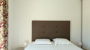 Una cama cuidadosamente tendida con un cabecero capitonado, ropa de cama blanca y dos lámparas de noche.