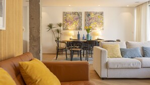 Una sala de estar moderna con un sofá, una mesa de comedor con sillas y dos cuadros abstractos en la pared.