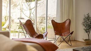 Un dormitorio moderno con un ventanal grande, dos sillones de cuero, una cama y una planta en maceta.