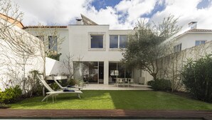 Una casa moderna con piscina, un patio con mobiliario exterior y un césped bien cuidado.