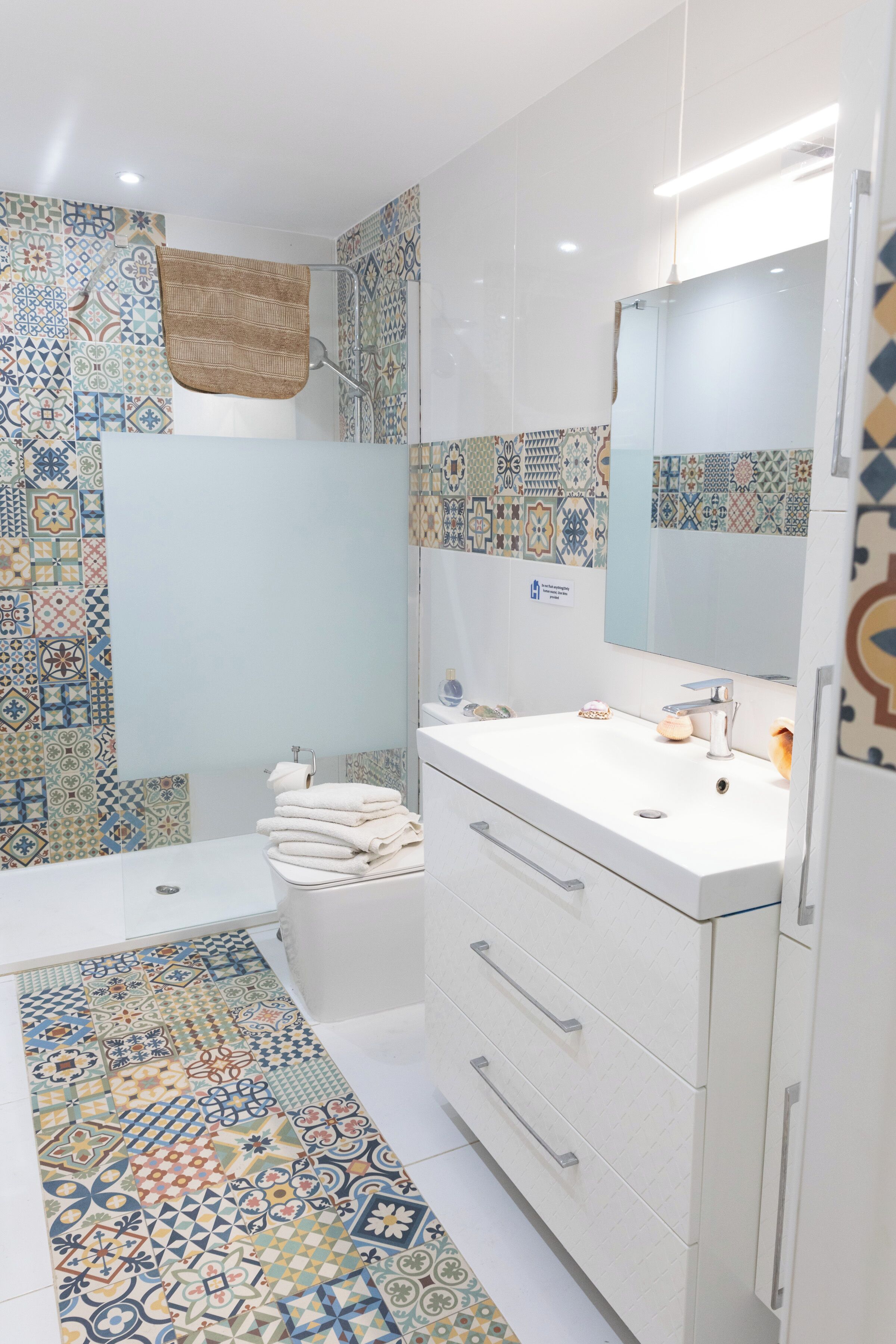 Un bagno moderno con piastrelle decorate, un lavandino bianco e uno specchio.