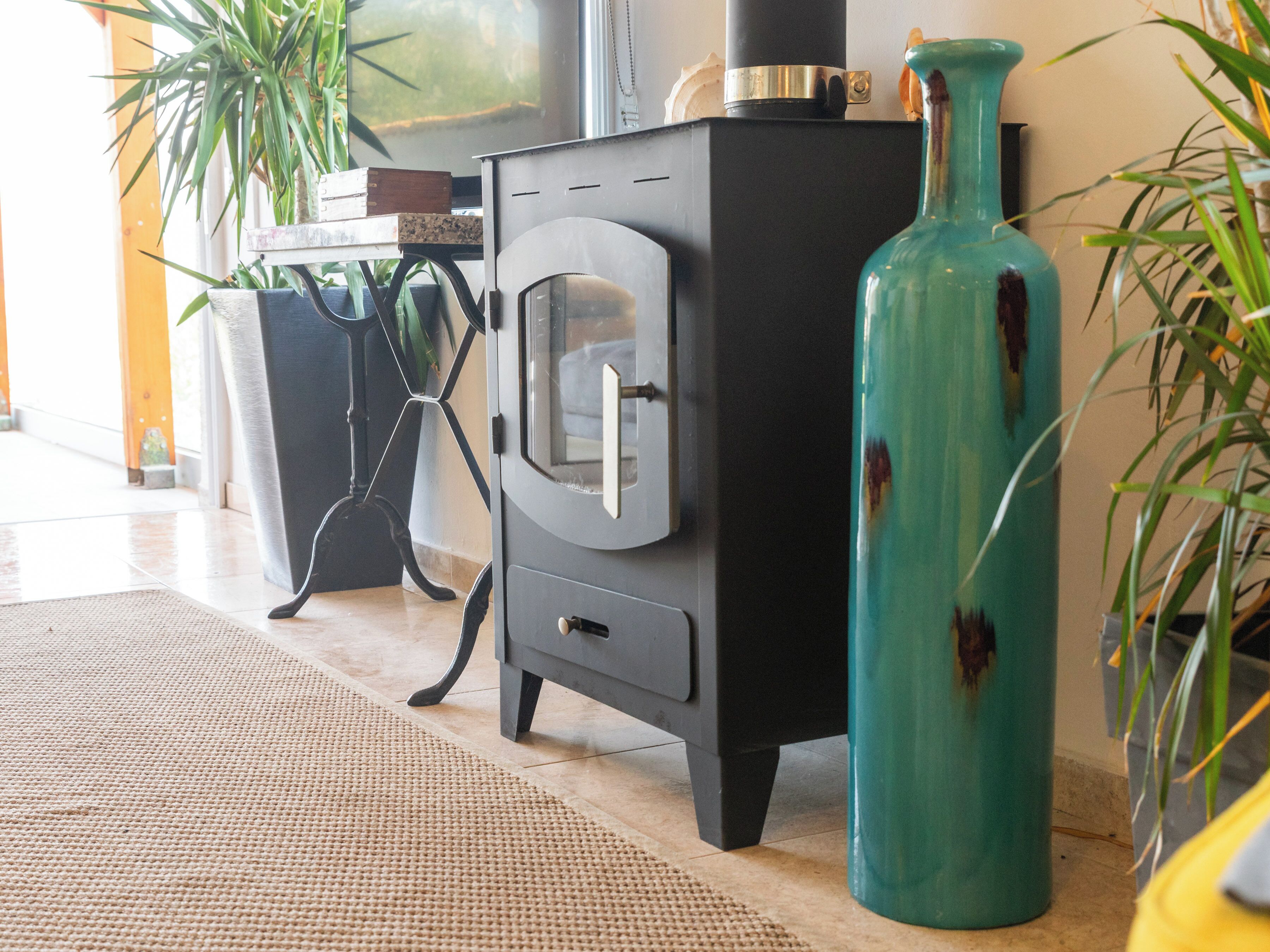 A room with a black wood-burning stove, a green vase, and potted plants.
