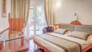Une chambre d’hôtel avec une table en verre, un lit doté de plusieurs oreillers, un ventilateur de plafond et une vue sur l’extérieur, visible à travers une porte vitrée.