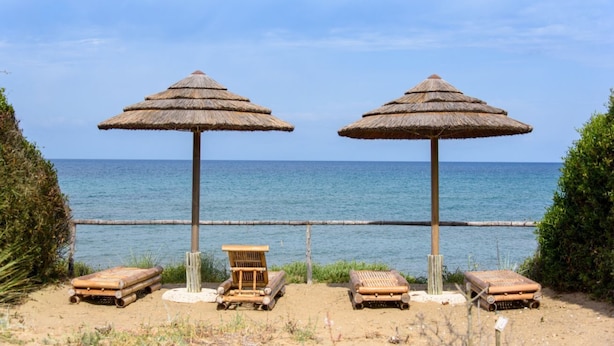 Une plage avec deux parasols en chaume et des chaises longues en bois.