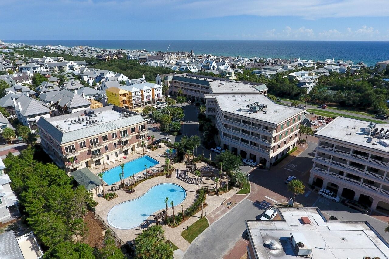 Aerial view of a coastal resort community featuring modern accommodations, swimming pools, and charming neighborhood buildings just steps from the ocean.