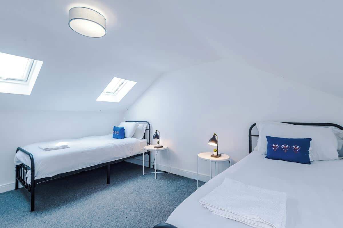 Une petite pièce bien éclairée, avec deux lits, une lucarne et une seule table de chevet avec une lampe.