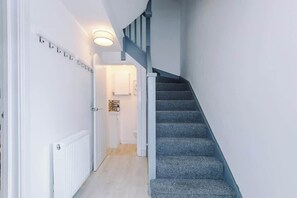 Eine Treppe mit Geländer und Teppichstufen führt zu einem Raum mit einer weißen Tür und einer Leuchte darüber.