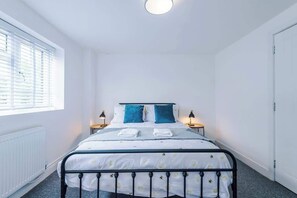 Ein Schlafzimmer mit einem Bett, zwei Nachttischlampen, einem Fenster mit Jalousien und einer Tür.