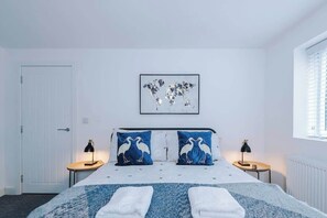 Un dormitorio con una cama, dos mesitas de noche, un mapa mundial enmarcado en la pared y una ventana con persianas.