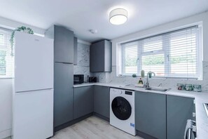 A modern kitchen with grey cabinets, a built-in washing machine, and a window with blinds.