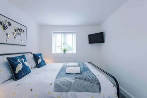 Une chambre à coucher avec un lit, des oreillers, une fenêtre, une plante et un téléviseur.