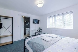 A modern bedroom with a bed, a desk, a TV, and a window with blinds.