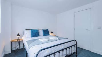 A bedroom with a bed, two bedside tables, a nightstand, a door, and a ceiling light fixture.
