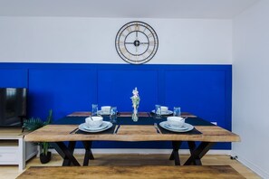 Ein Essbereich mit einem Holztisch, gedeckt für vier Personen, einer dekorativen Vasen-Mitte und einer an der Wand montierten Uhr.