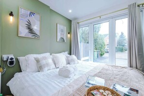Hotelkamer met een bed, een weegschaal op het nachtkastje, een raam met gordijnen en een wandlamp.