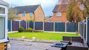 A residential backyard with a paved patio, a small lawn, and a wooden fence.