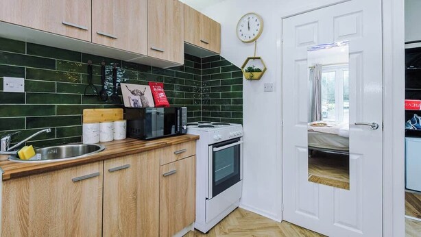 A compact kitchen with wooden cabinets, a microwave, stove, and a sink. - NEW! Preston Central & Sleek Studio | Wifi Parking (Fulwood)