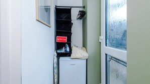 A small room with a white refrigerator, a shoe rack with black bags, and a window with a view of trees.