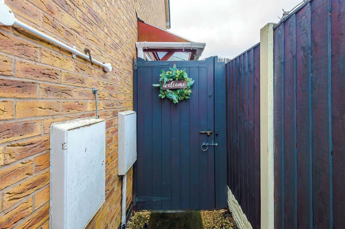 A dark blue gate with a 'welcome' sign and a wreath, a brick wall, and a metal electrical box.