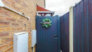 A dark blue gate with a 'welcome' sign and a wreath, a brick wall, and a metal electrical box.