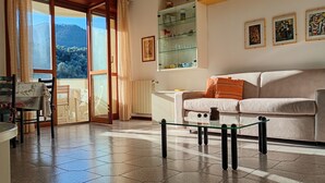 Un salon comprenant un canapé, une table basse en verre et une vue sur un paysage montagneux, visible à travers une grande fenêtre.