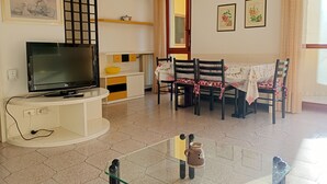 Un salon avec un téléviseur, une table à manger avec des chaises, un comptoir de cuisine et un escalier.