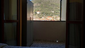 Une chambre avec un lit, une armoire et une fenêtre donnant sur une montagne et des bâtiments.