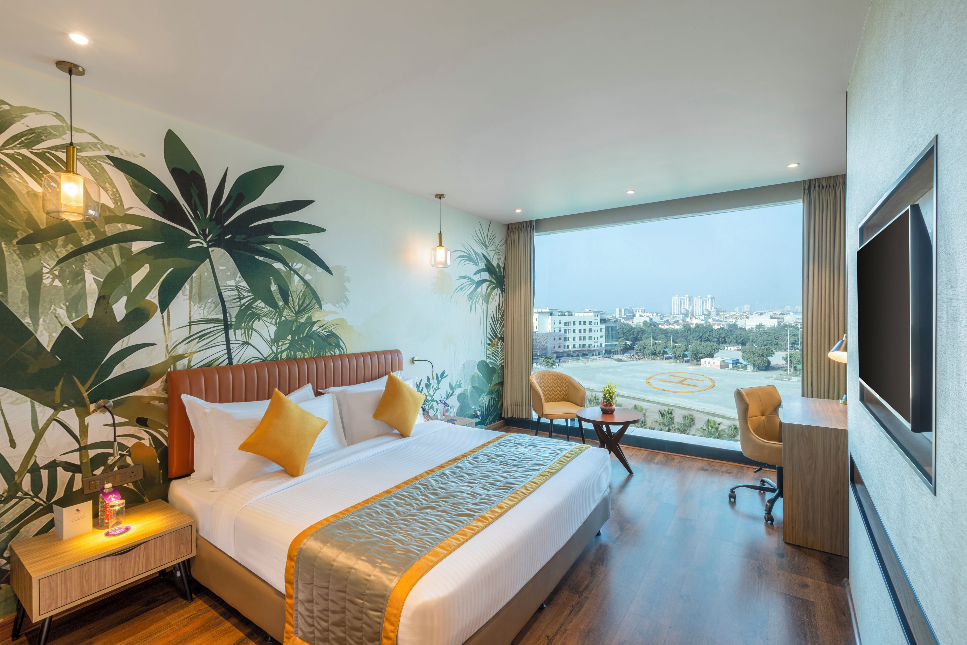 A hotel room with a large bed, a desk, a chair, a TV, and a view of the city.