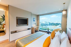 A hotel room with a bed, a desk, a TV, a window with a city view, and a balcony.