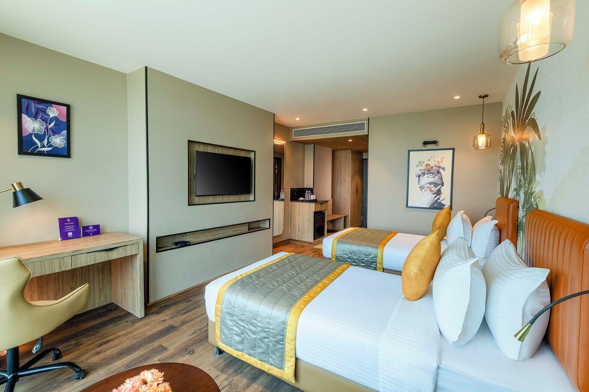 Ein Hotelzimmer mit zwei Betten, einem Schreibtisch, einem Fernseher und einer kleinen Küchenzeile.