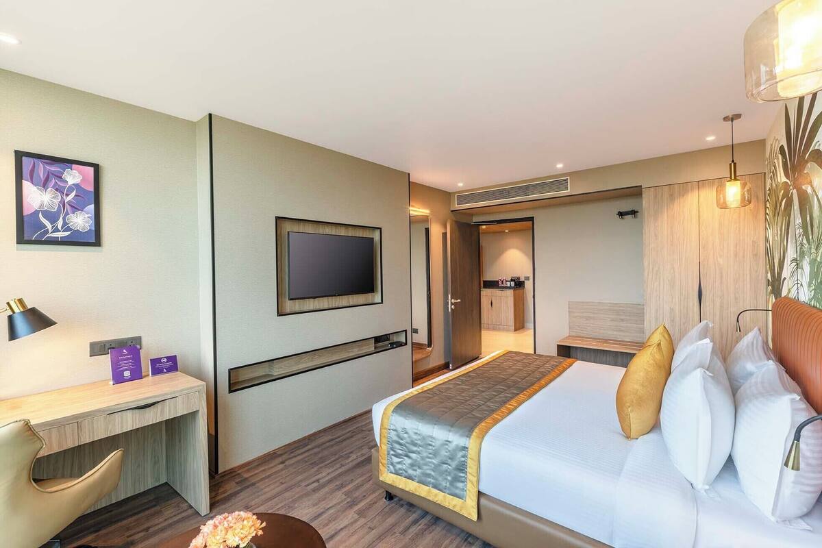 A hotel room with a bed, a desk, a TV, and a bathroom visible through an open door.