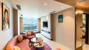 Una sala de estar moderna con un sofá, una mesa de centro con fruta, un televisor y vistas a la ciudad.