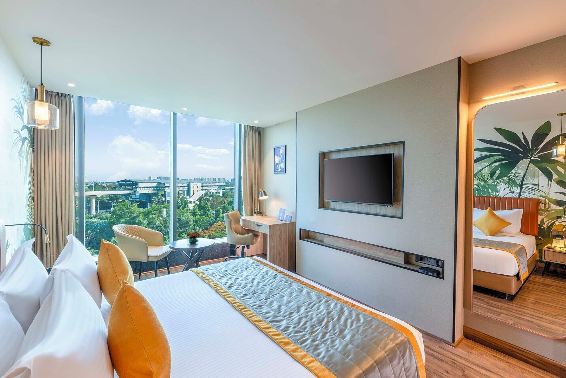 A hotel room with a large bed, a TV, a desk with a lamp, and a view of the city.