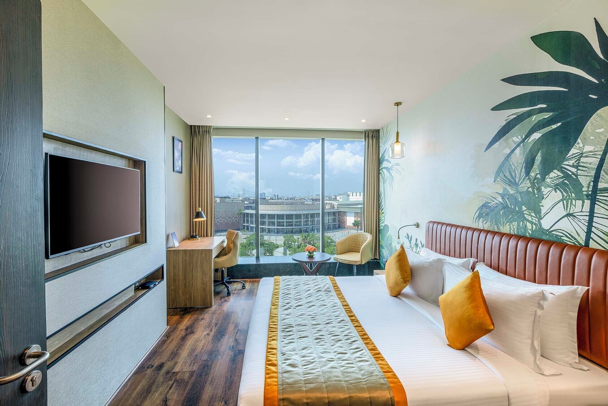 A hotel room with a bed, a desk, a chair, a TV, and a large window with a city view.
